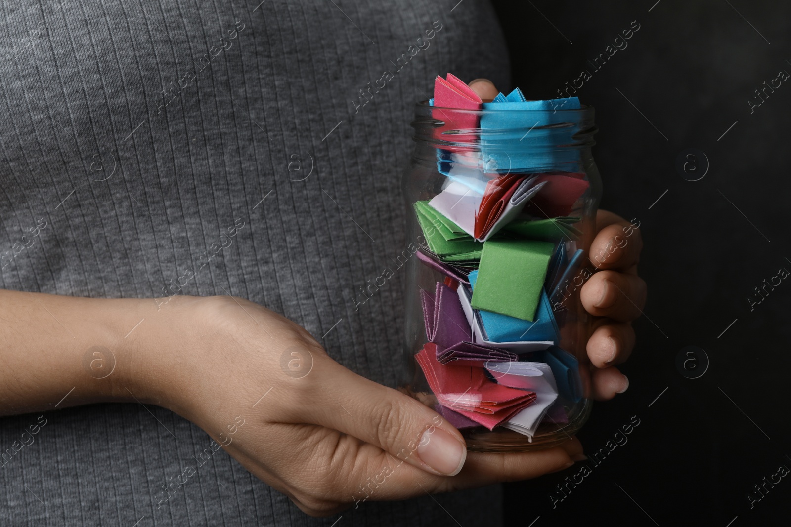 Photo of Woman holding glass jar with colorful paper pieces, closeup on hands