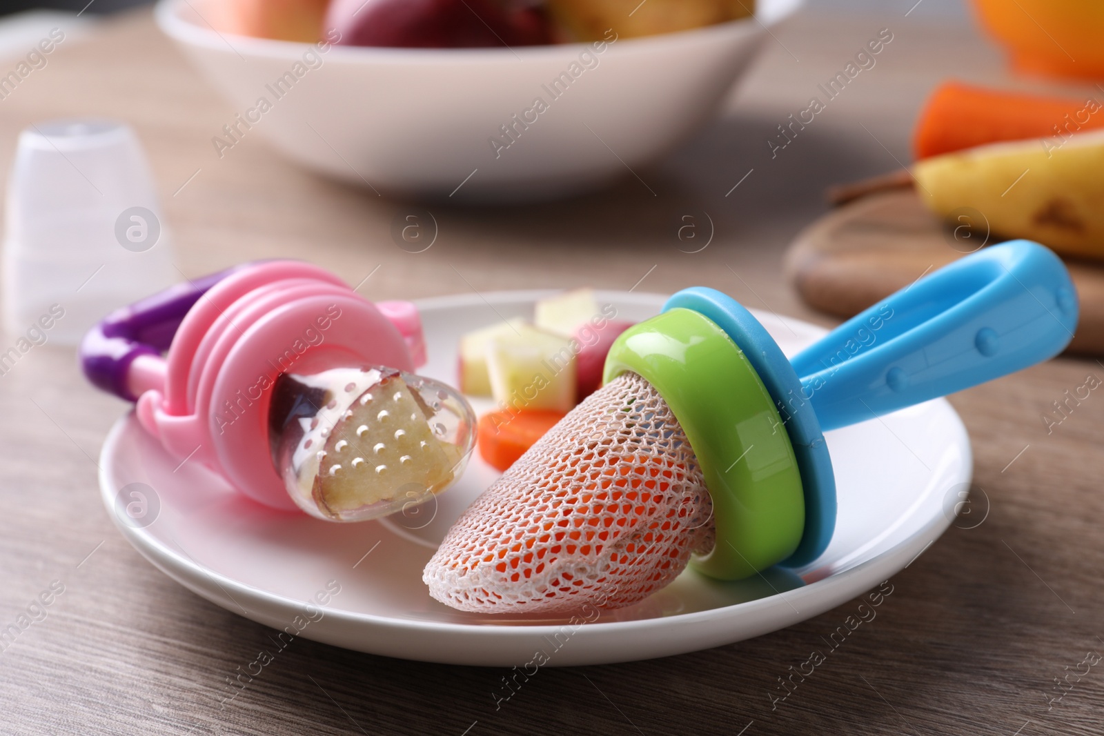 Photo of Different nibblers with fresh apple and boiled carrot on wooden table, closeup. Baby feeder