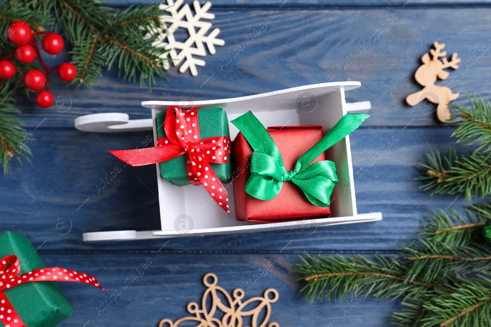 Photo of Flat lay composition with sleigh, fir tree branches and gift boxes on blue wooden table