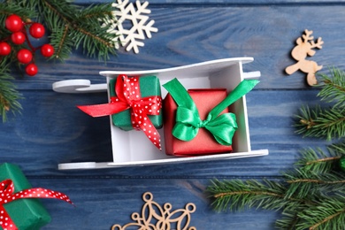 Photo of Flat lay composition with sleigh, fir tree branches and gift boxes on blue wooden table