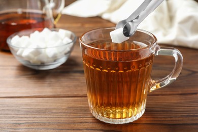 Photo of Adding sugar cube into cup of tea at wooden table, closeup