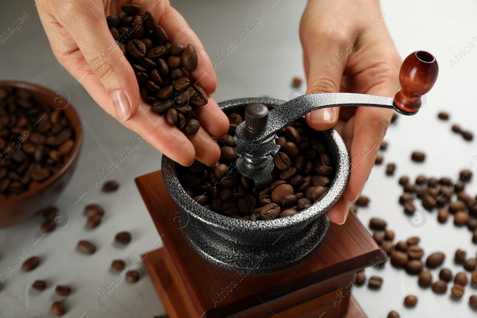 Photo of Woman using manual coffee grinder at light grey table, closeup