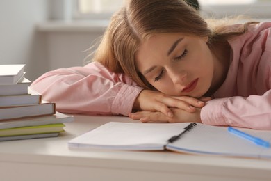 Young tired woman sleeping near books at white table indoors