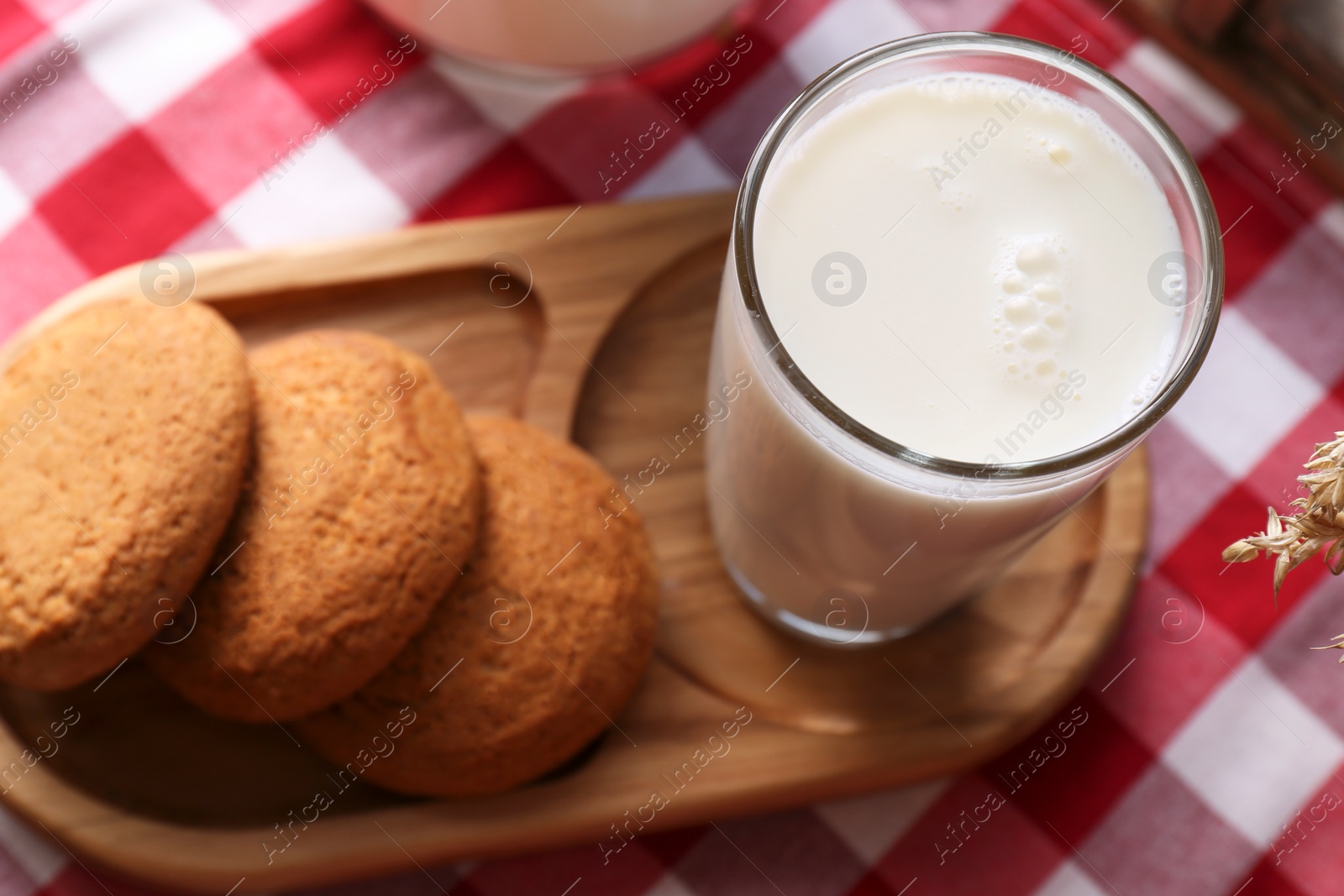 Photo of Glass of milk with cookies on red checkered tablecloth, closeup