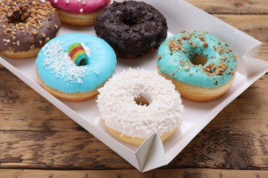 Photo of Box with different tasty glazed donuts on wooden table, closeup