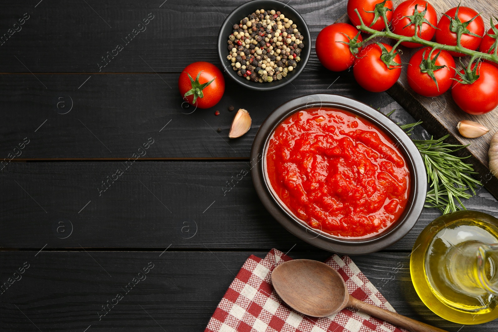 Photo of Homemade tomato sauce in bowl, spoon and fresh ingredients on black wooden table, flat lay. Space for text