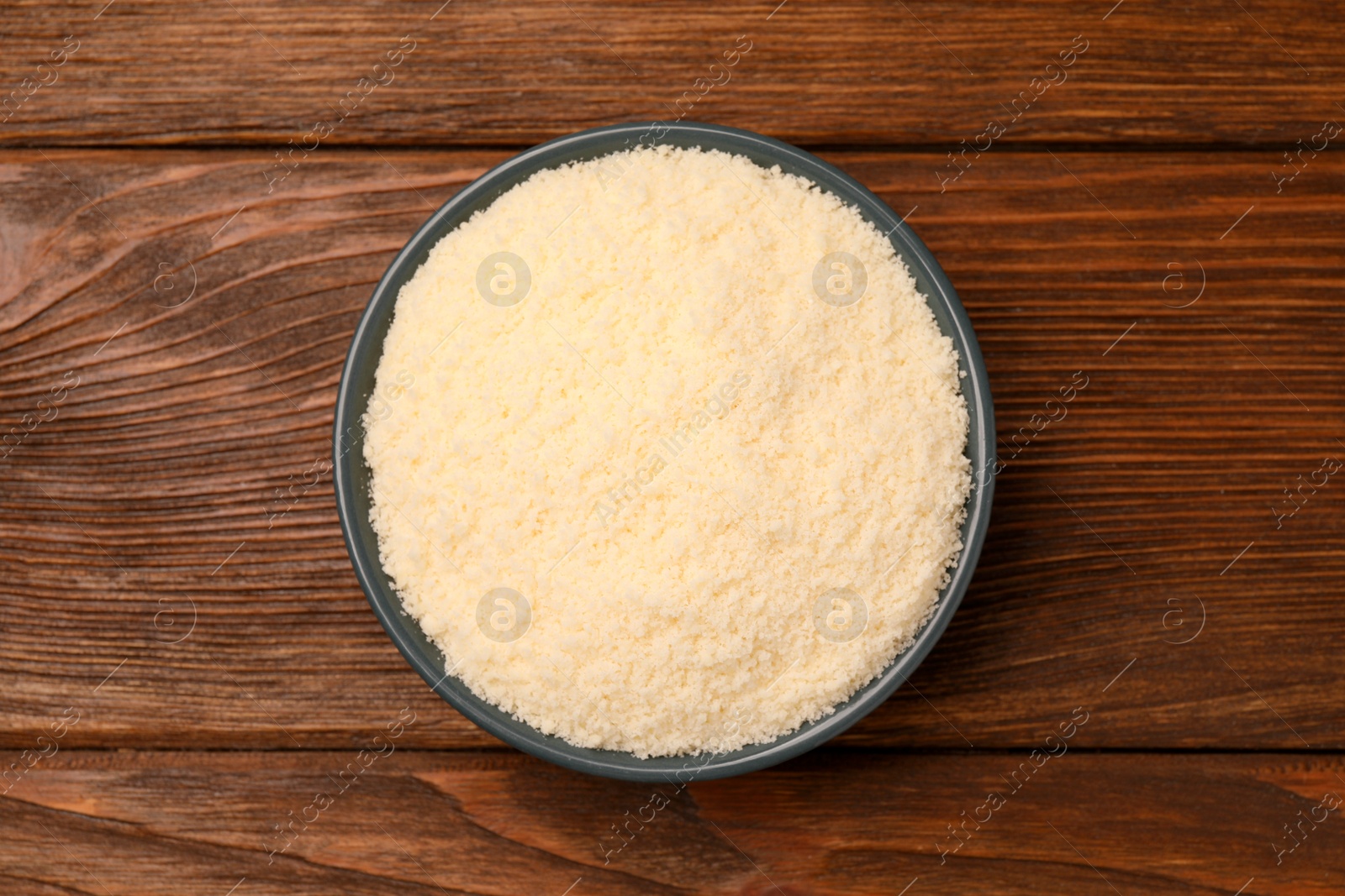 Photo of Delicious grated parmesan cheese in bowl on wooden table, top view