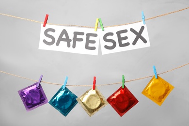 Paper sheets with words SAFE SEX and colorful condoms hanging on clothesline against light grey background