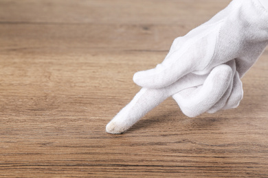 Photo of Person in white glove checking cleanliness of wooden  table, closeup