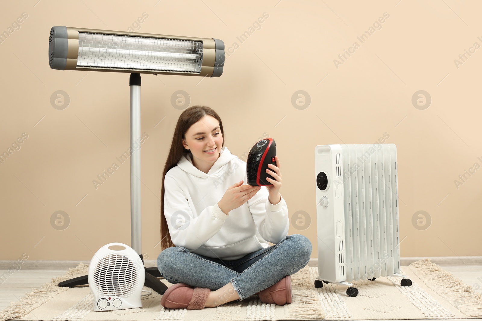 Photo of Young woman with different modern electric heaters near beige wall indoors