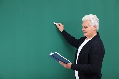 Photo of Portrait of senior teacher with book and chalk at green board, space for text