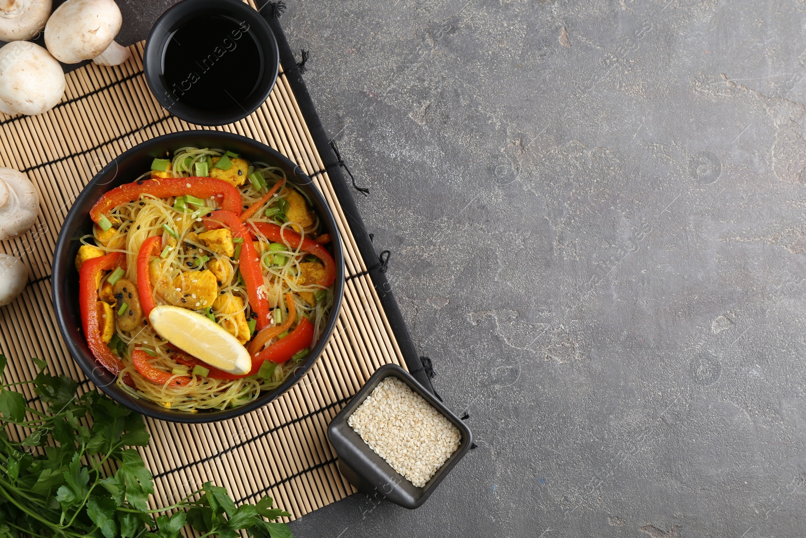 Photo of Stir-fry. Delicious cooked noodles with chicken and vegetables in bowl served on gray textured table, flat lay. Space for text