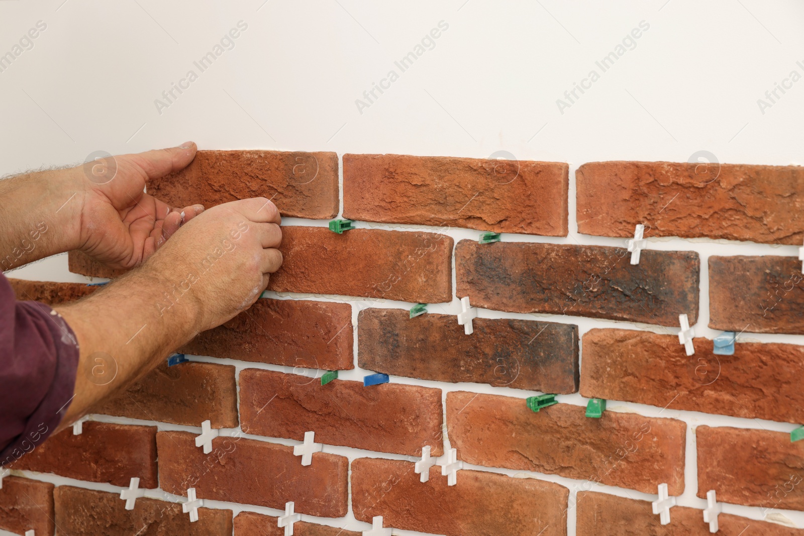 Photo of Professional builder installing new brown decorative bricks on wall, closeup