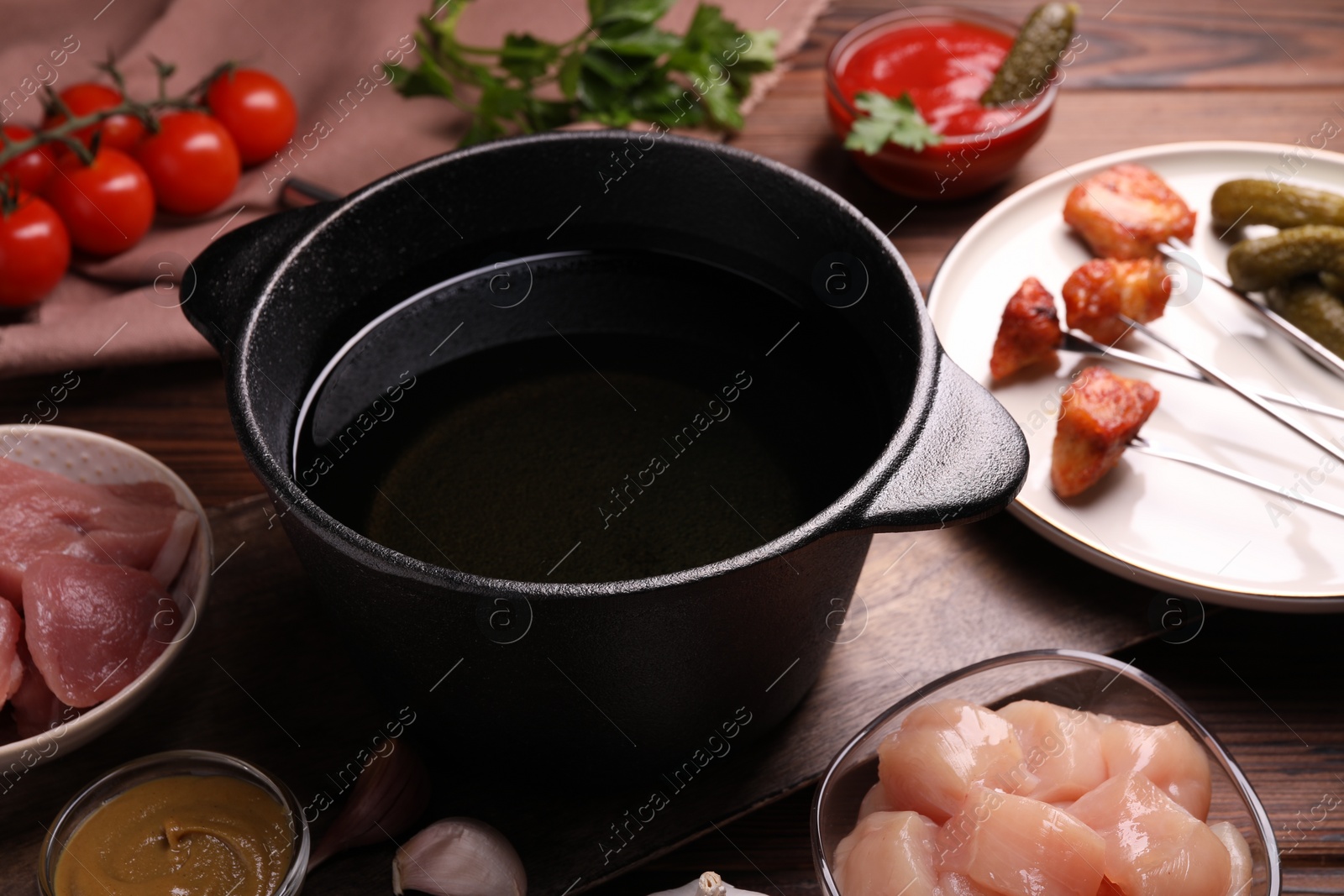 Photo of Fondue pot, forks with fried meat pieces and other products on wooden table