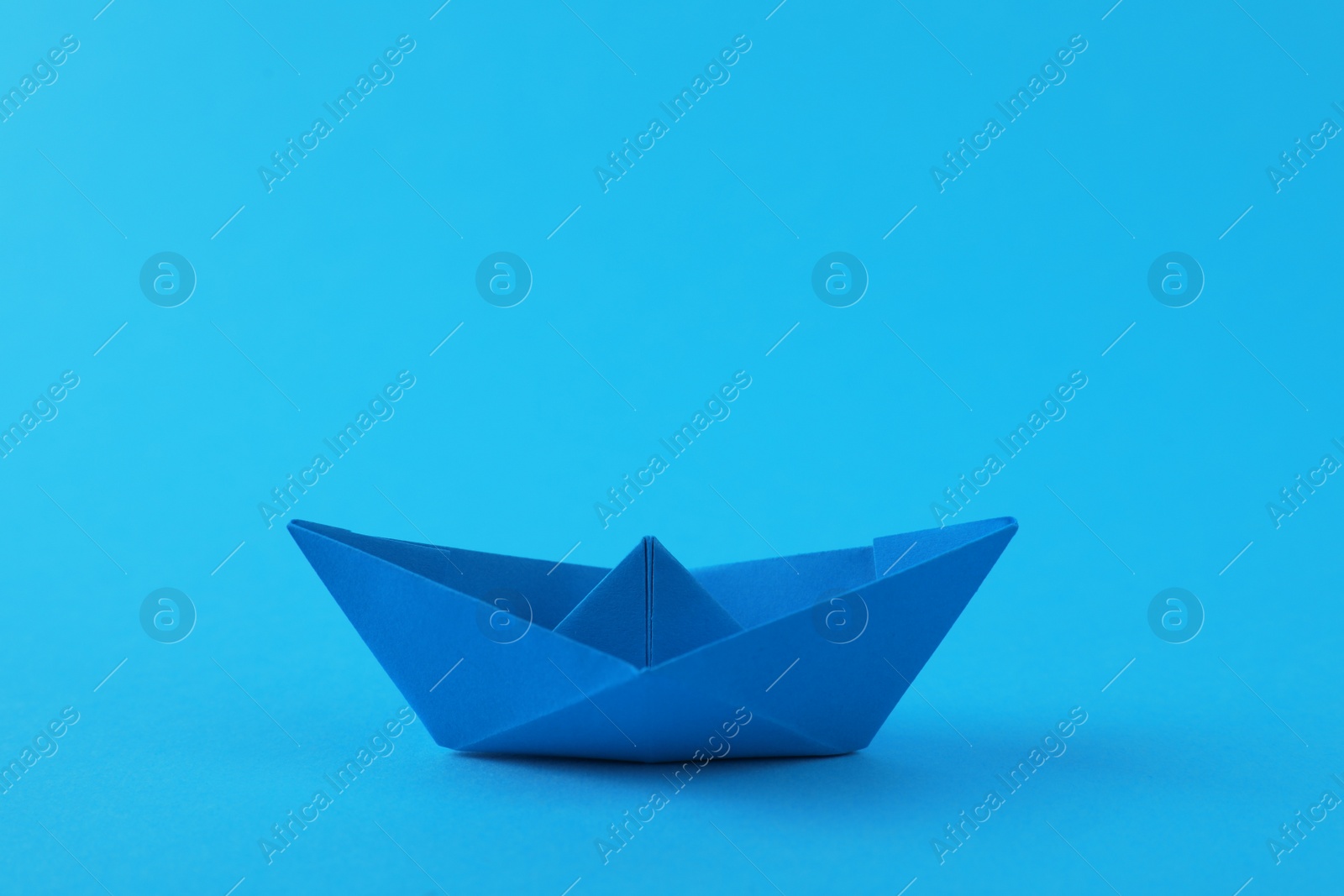 Photo of Handmade paper boat on light blue background. Origami art