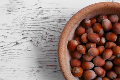 Photo of Bowl with hazelnuts and leaves on white wooden table, top view. Space for text