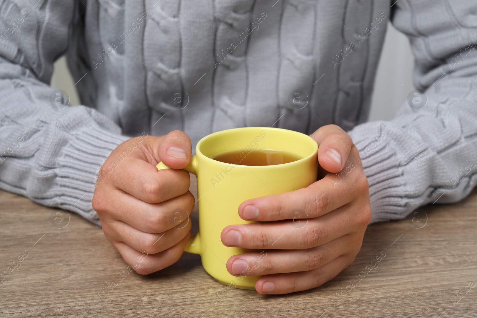 Photo of Man with yellow mug at wooden table, closeup