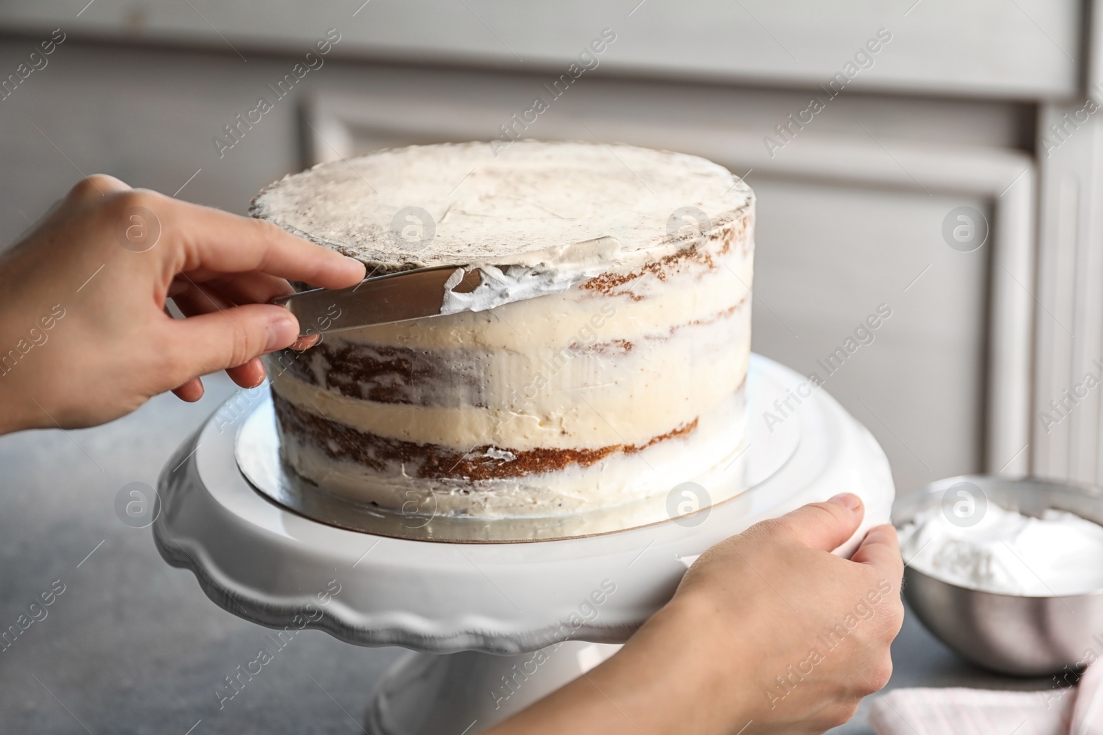 Photo of Woman decorating delicious cake with fresh cream on stand. Homemade pastry