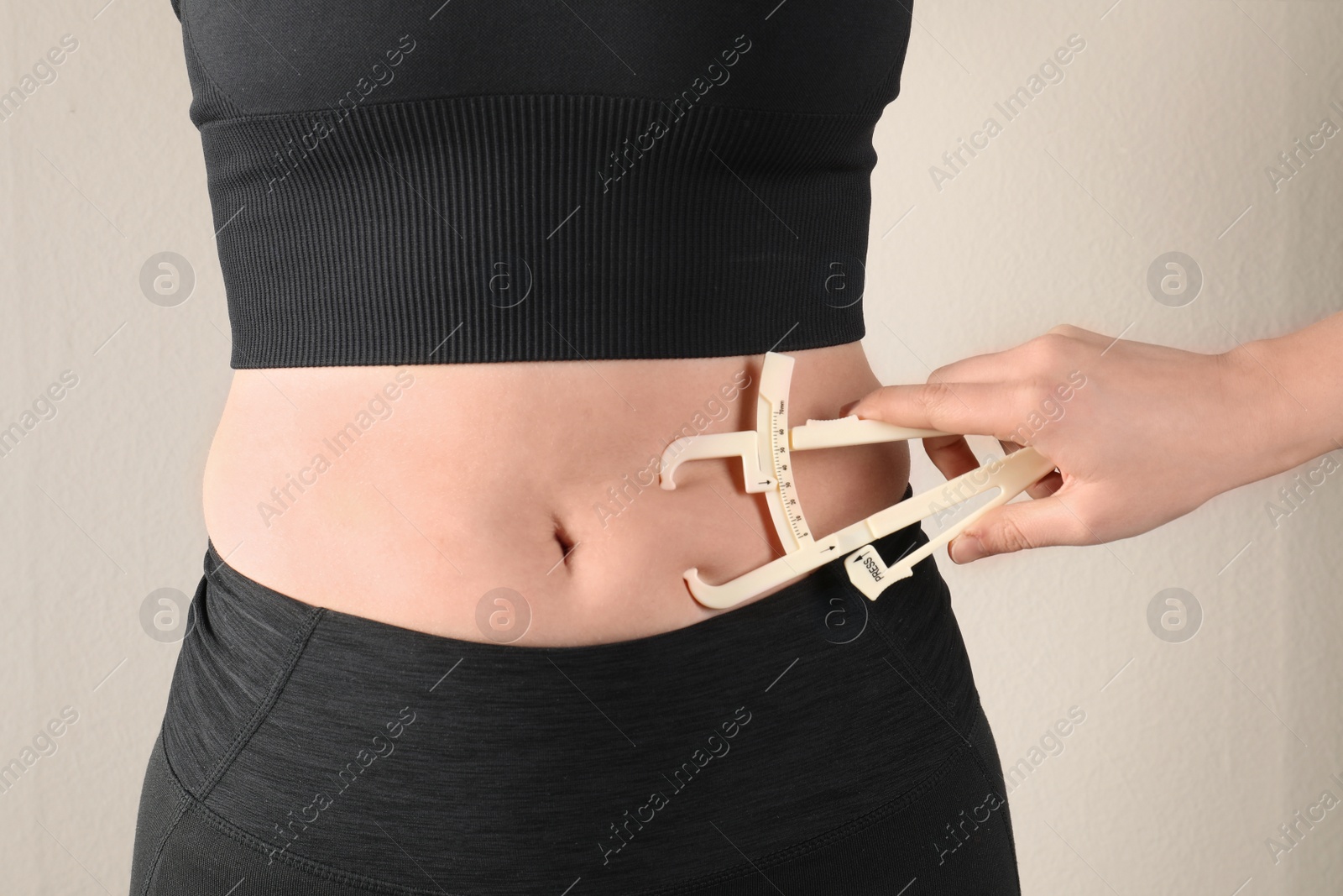 Photo of Nutritionist measuring woman's body fat layer with caliper on beige background, closeup