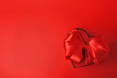 Beautiful heart shaped gift box with bow on red background, top view. Space for text