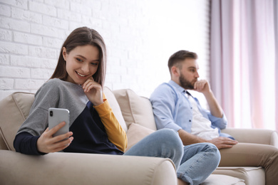 Photo of Young woman with smartphone ignoring her boyfriend at home. Relationship problems