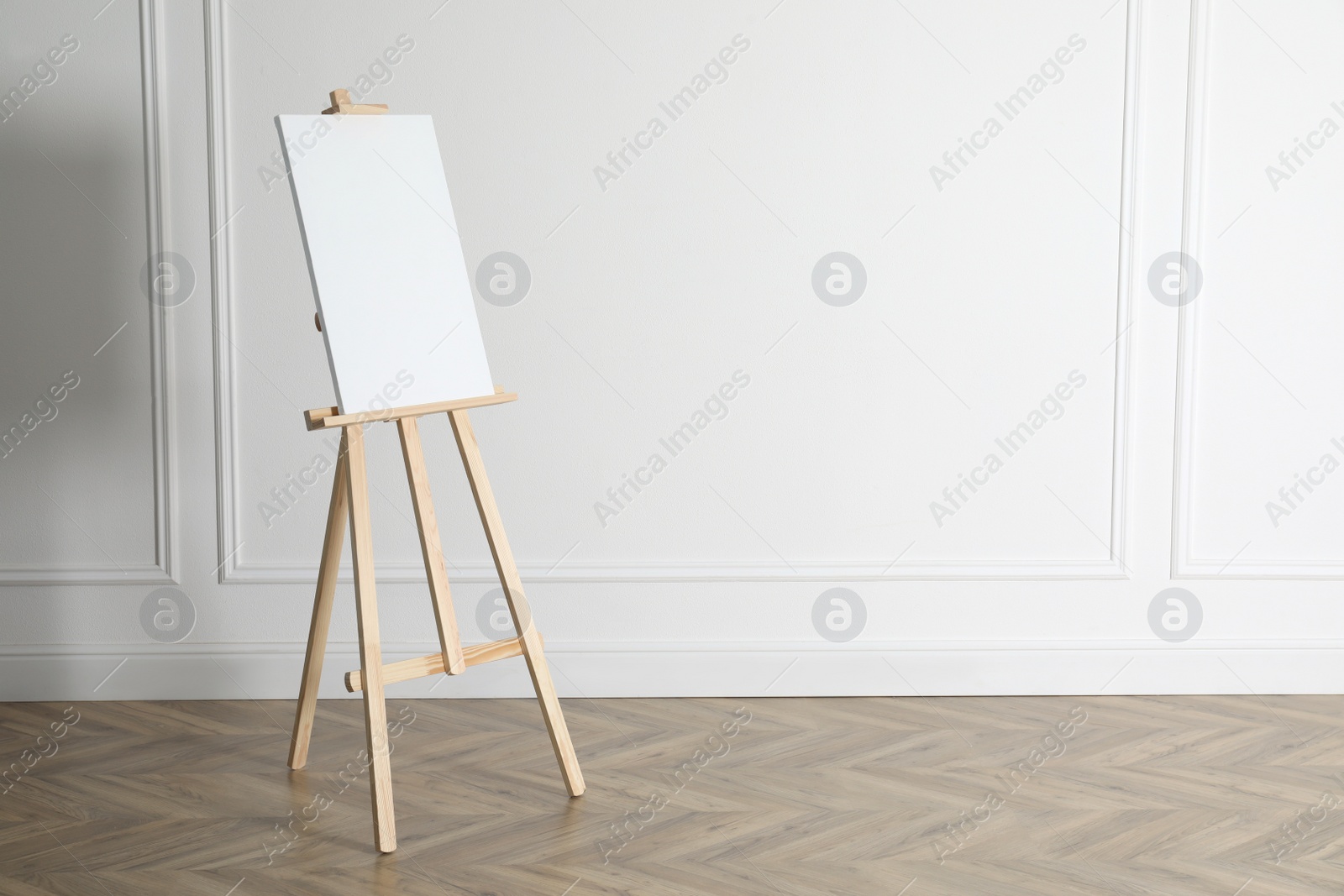 Photo of Wooden easel with blank canvas near light wall. Space for text