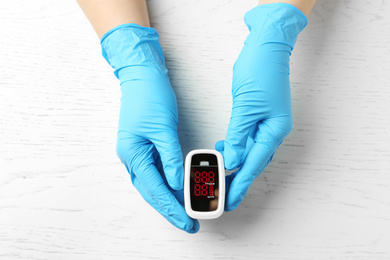 Photo of Doctor in latex gloves holding fingertip pulse oximeter on white wooden background, top view