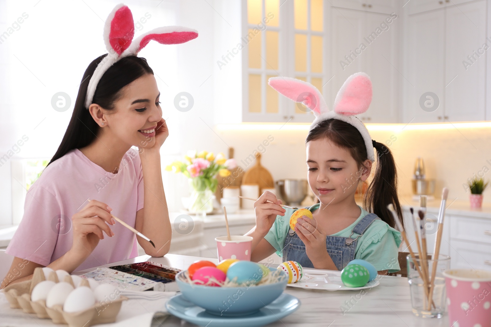 Photo of Happy mother with her cute daughter painting Easter eggs at table in kitchen