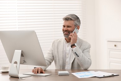 Photo of Professional accountant talking on phone and working at wooden desk in office