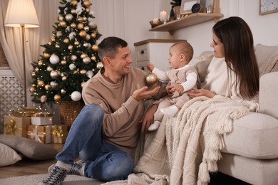 Photo of Happy couple with cute baby in room decorated for Christmas