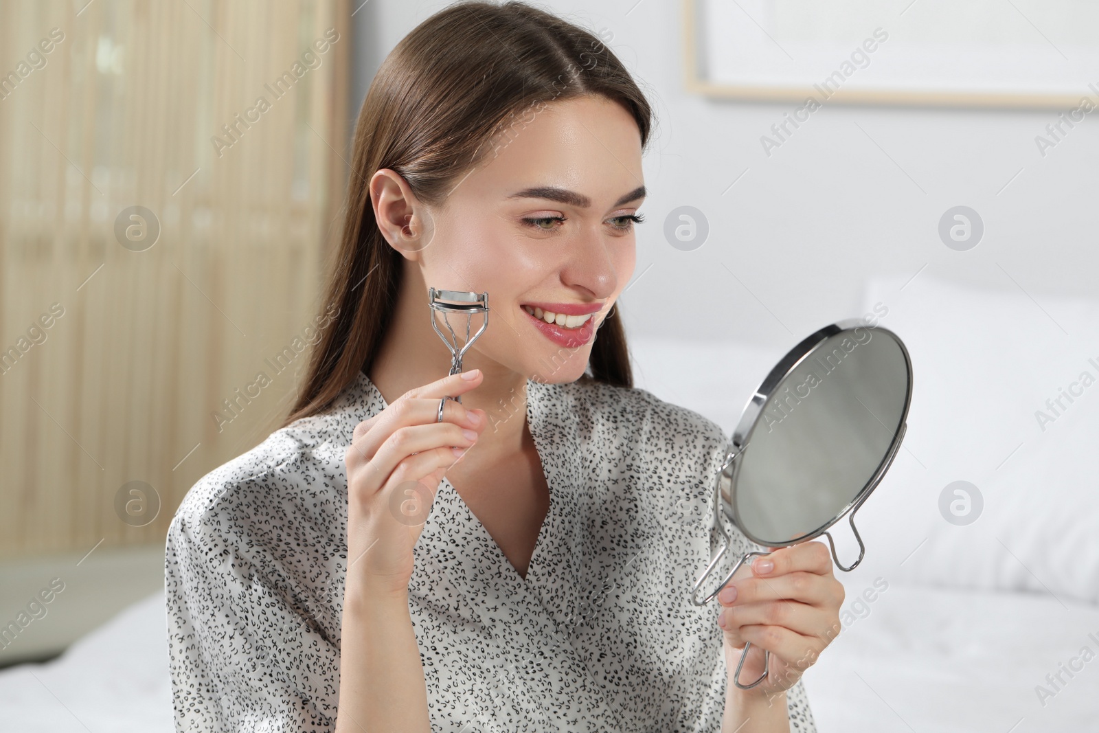 Photo of Woman with eyelash curler near mirror at home