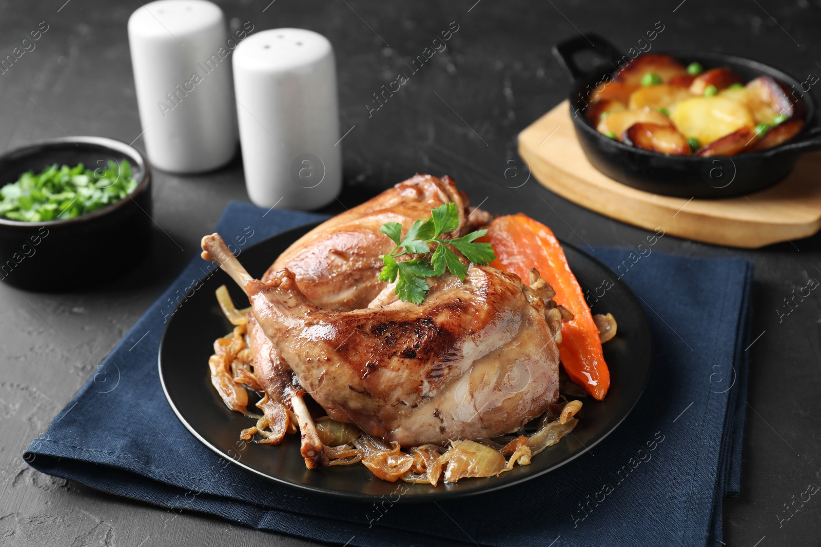 Photo of Tasty cooked rabbit meat with vegetables served on black table