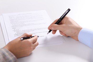 Photo of Businesspeople signing contract at white table, closeup of hands