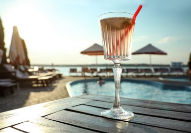 Glass of fresh summer cocktail on wooden table near swimming pool outdoors, low angle view