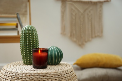 Decorative ceramic cacti and burning candle on wicker stand indoors, space for text. Interior design