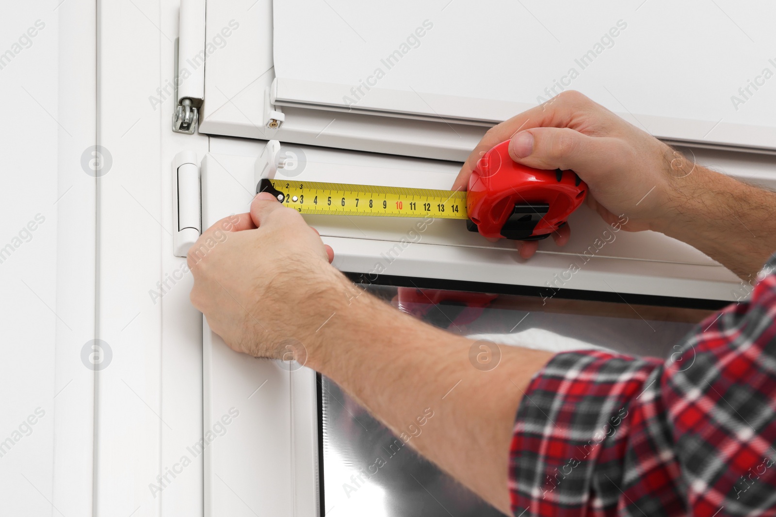 Photo of Worker using measuring tape while installing roller window blind indoors, closeup
