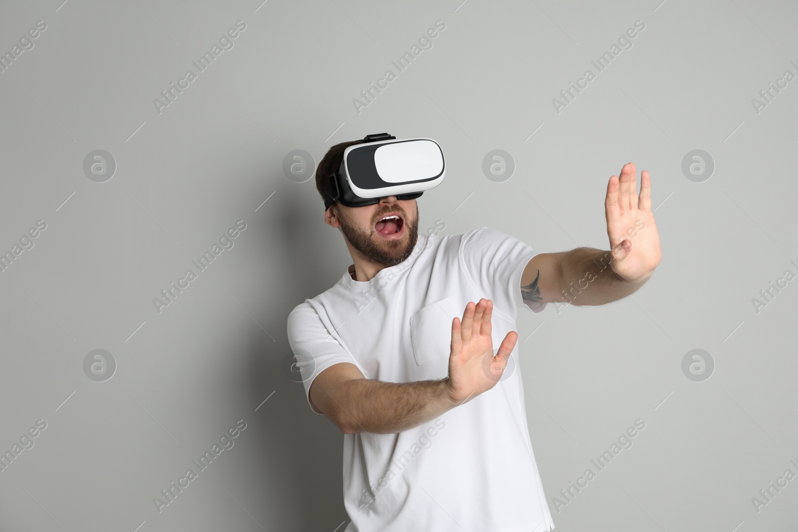 Photo of Emotional man using virtual reality headset on light grey background