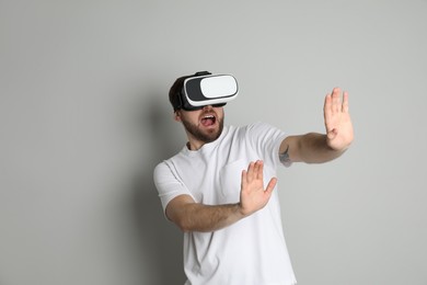 Photo of Emotional man using virtual reality headset on light grey background