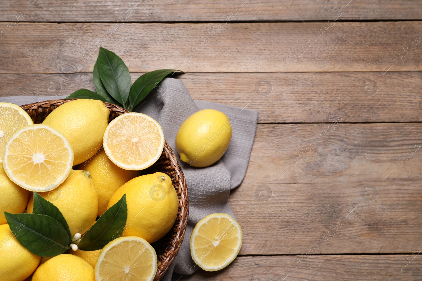 Photo of Many fresh ripe lemons with green leaves on wooden table, flat lay. Space for text