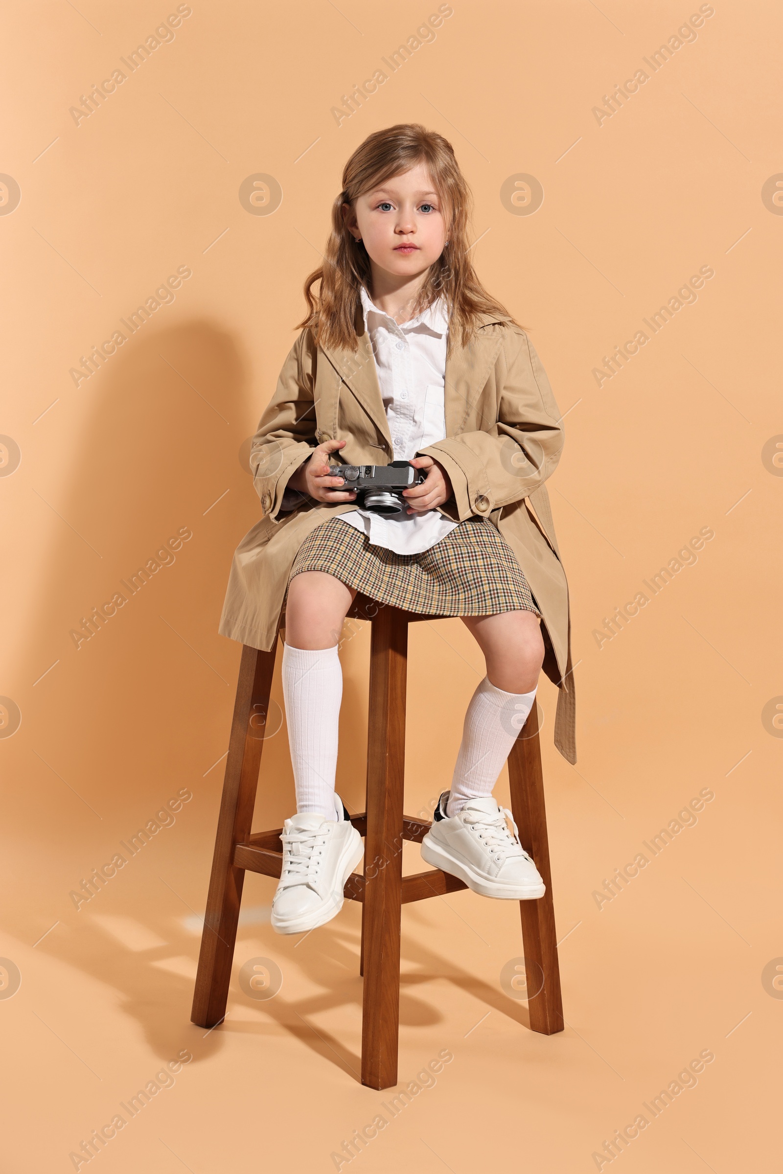 Photo of Fashion concept. Stylish girl with vintage camera on pale orange background