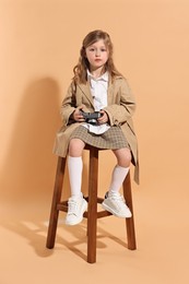 Fashion concept. Stylish girl with vintage camera on pale orange background
