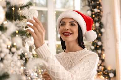 Photo of Happy young woman decorating Christmas tree at home