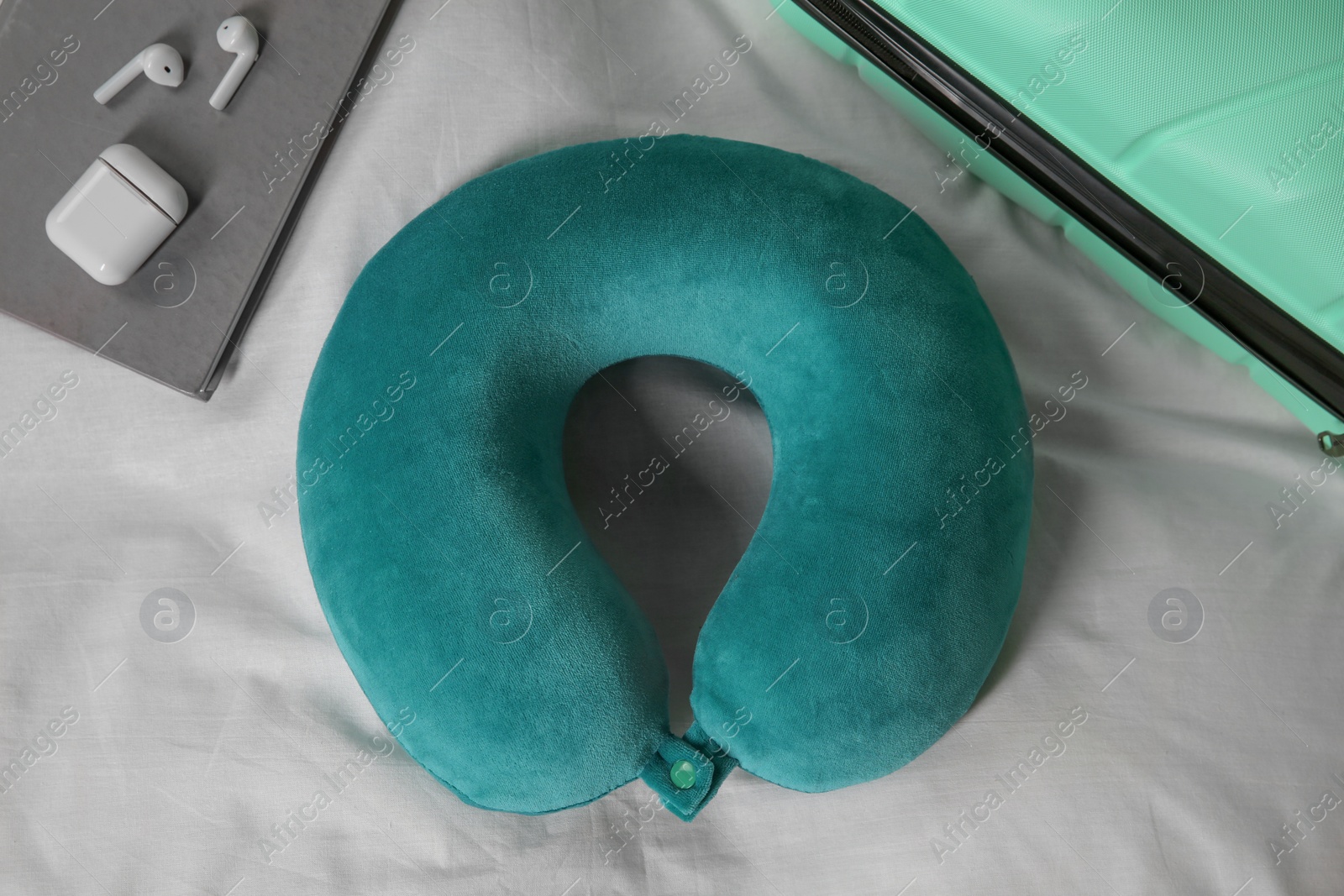 Photo of Turquoise travel pillow, suitcase, notebook and earphones on bed, flat lay