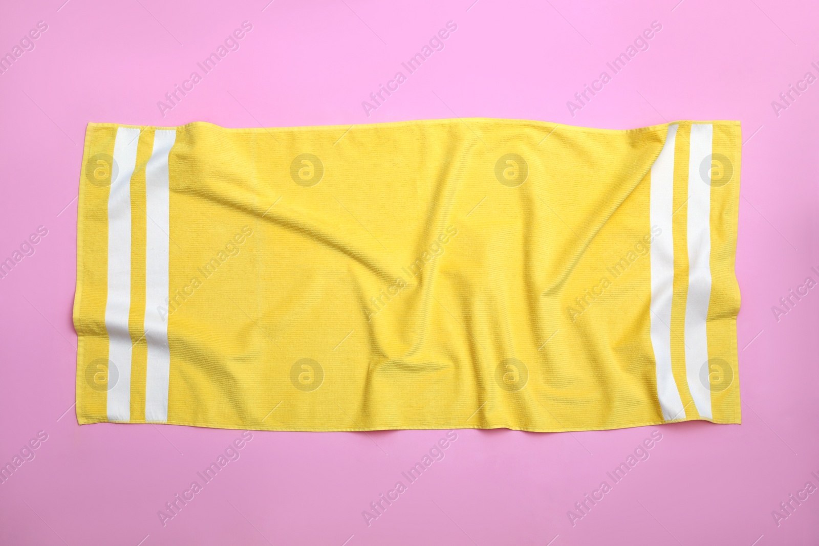 Photo of Crumpled yellow beach towel on pink background, top view