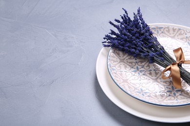 Photo of Bouquet of beautiful preserved lavender flowers and plates on light grey textured table, space for text