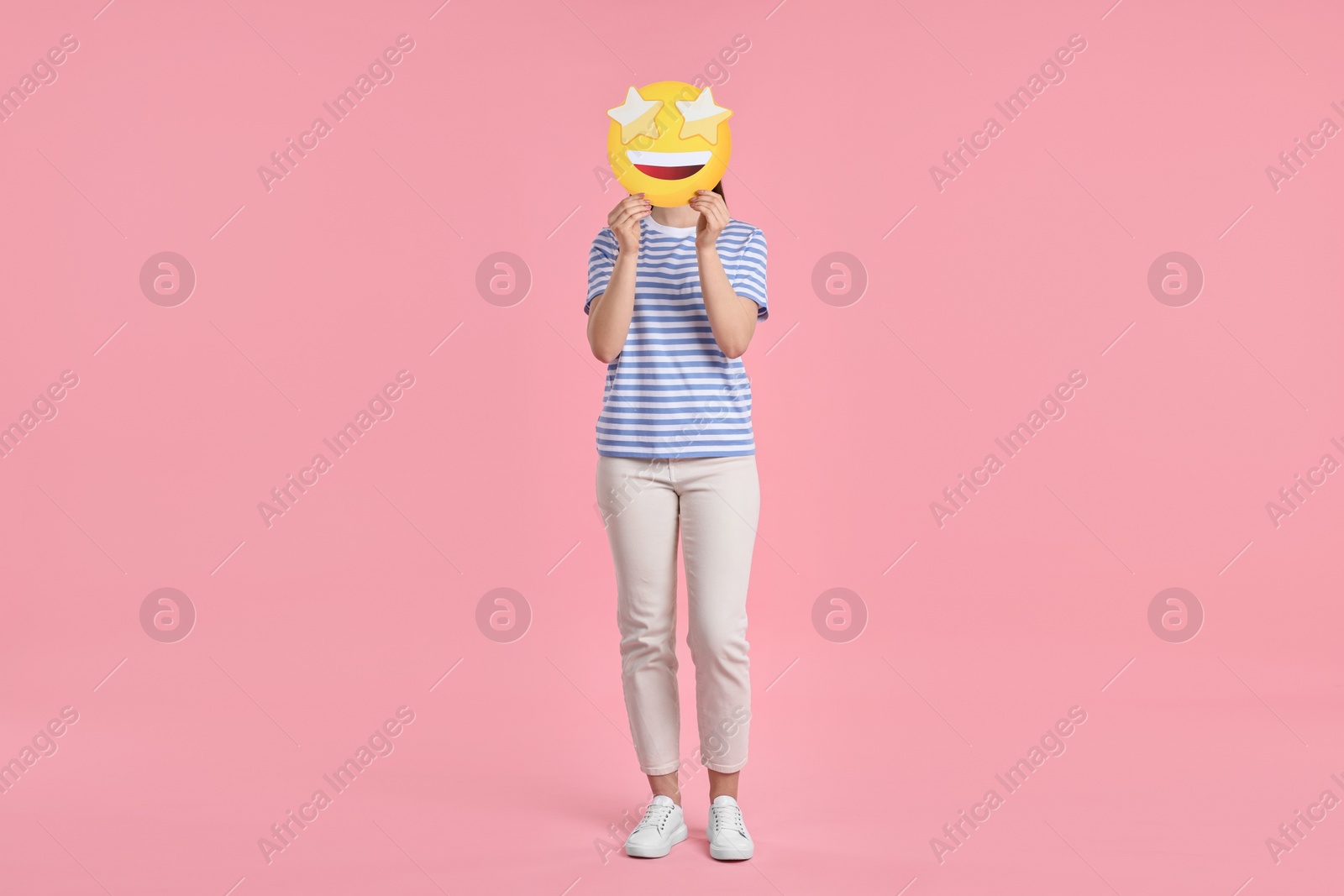 Photo of Woman holding emoticon with stars instead of eyes on pink background