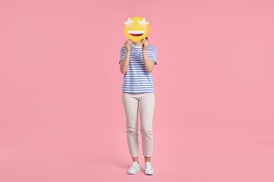 Photo of Woman holding emoticon with stars instead of eyes on pink background