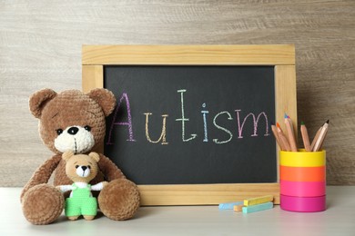 Photo of Small blackboard with word Autism, toys and stationery on wooden table