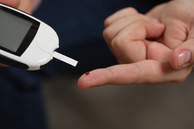 Photo of Diabetes test. Man checking blood sugar level with glucometer on blurred background, closeup