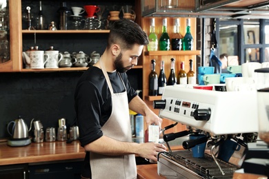 Photo of Barista pouring milk into metal jug near coffee machine at bar